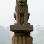 A stone statue of a lion sitting on its hind quarters atop a pillar.