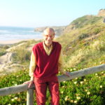A man leans back against a railing within a rugged coastal landscape.