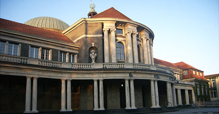 Large, pillared, grey building with a crimson roof.