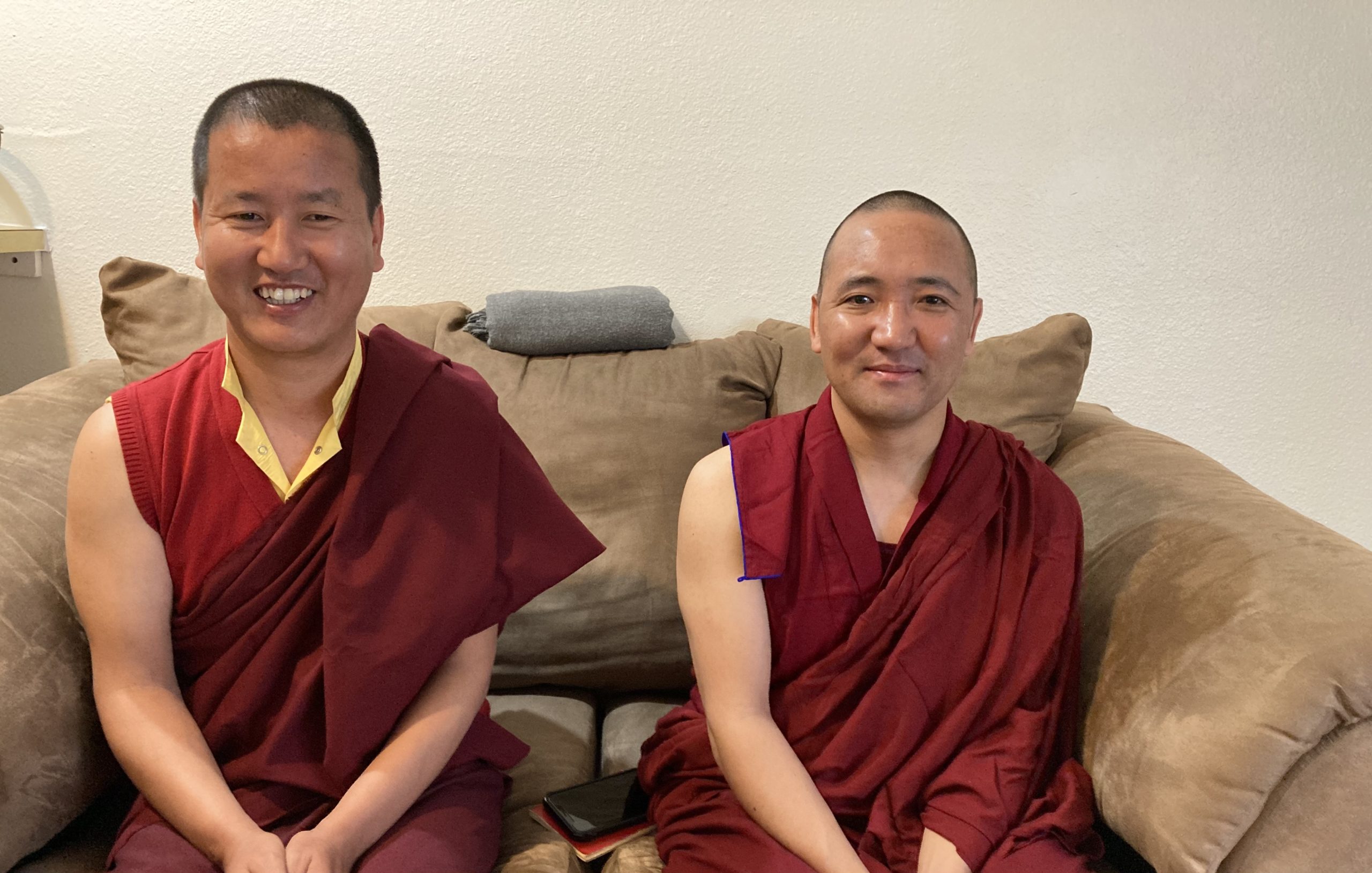 Two cheerful men in red robes are sitting on a brown sofa.