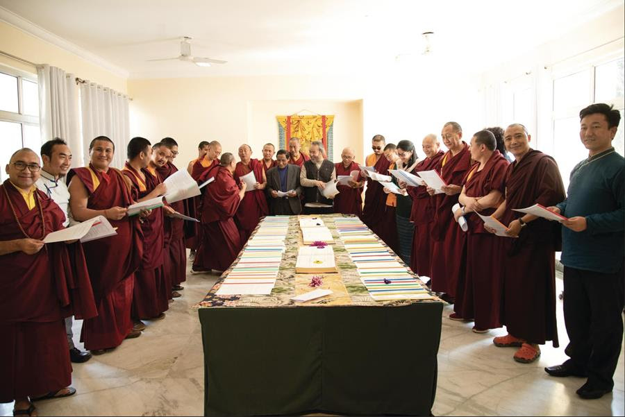 A large table in the middle, surrounded by four laypeople and numerous red-robed monks who are all holding white papers.