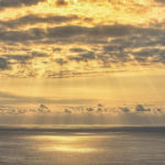 A gorgeous sunset begins over the ocean with clouds in the distance