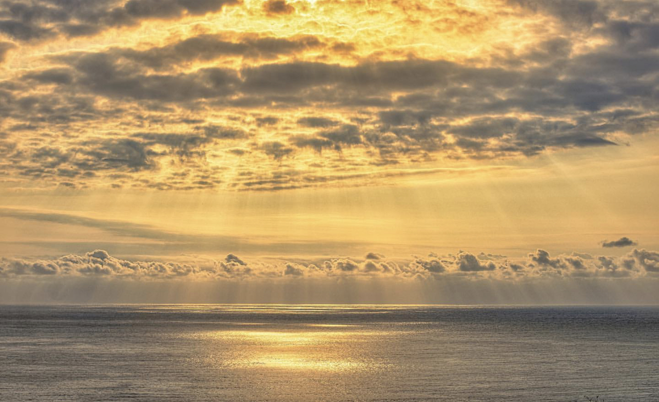 A gorgeous sunset begins over the ocean with clouds in the distance
